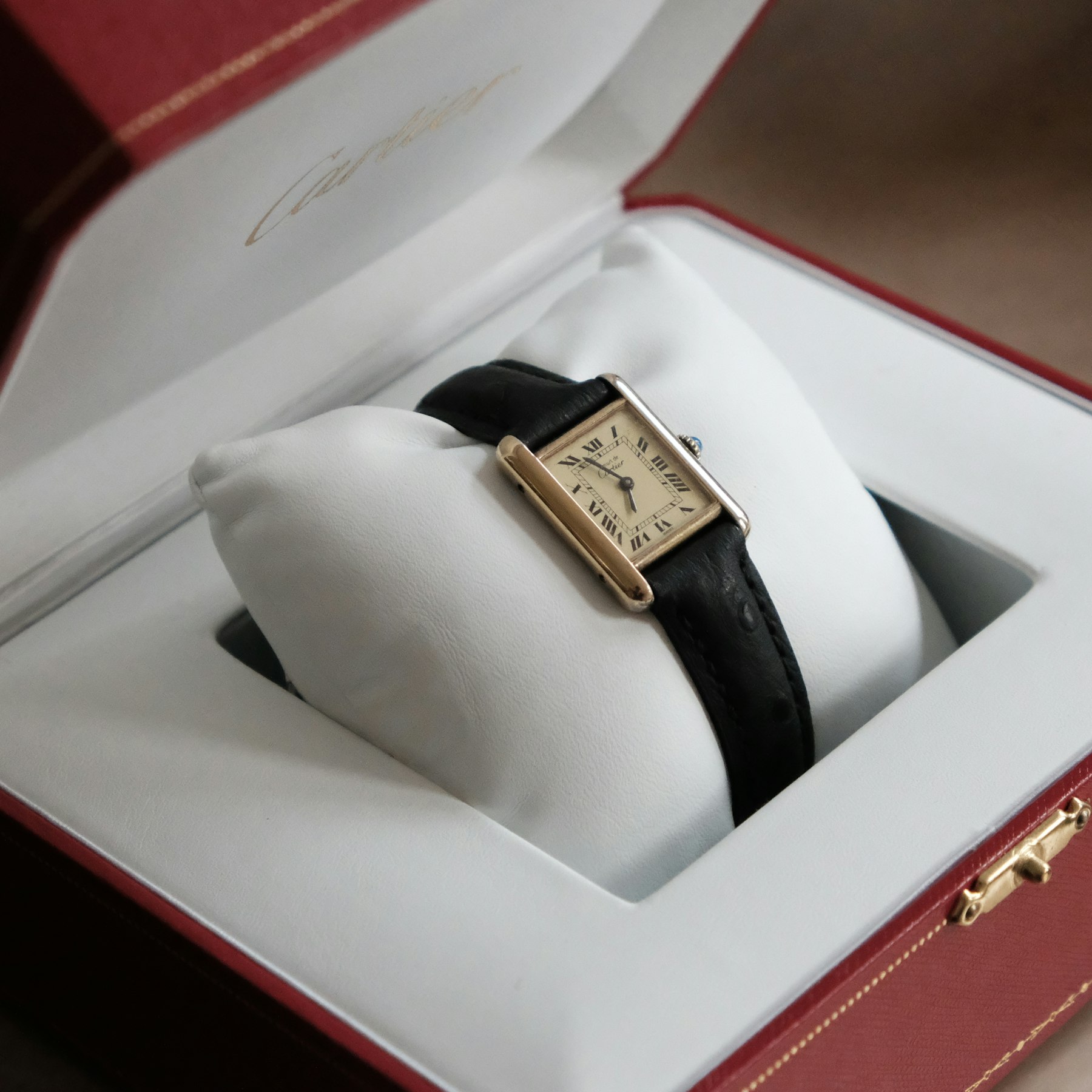 Gold-tone Tank Must de Cartier with cream Roman-numeral dial and black leather strap in its presentation box