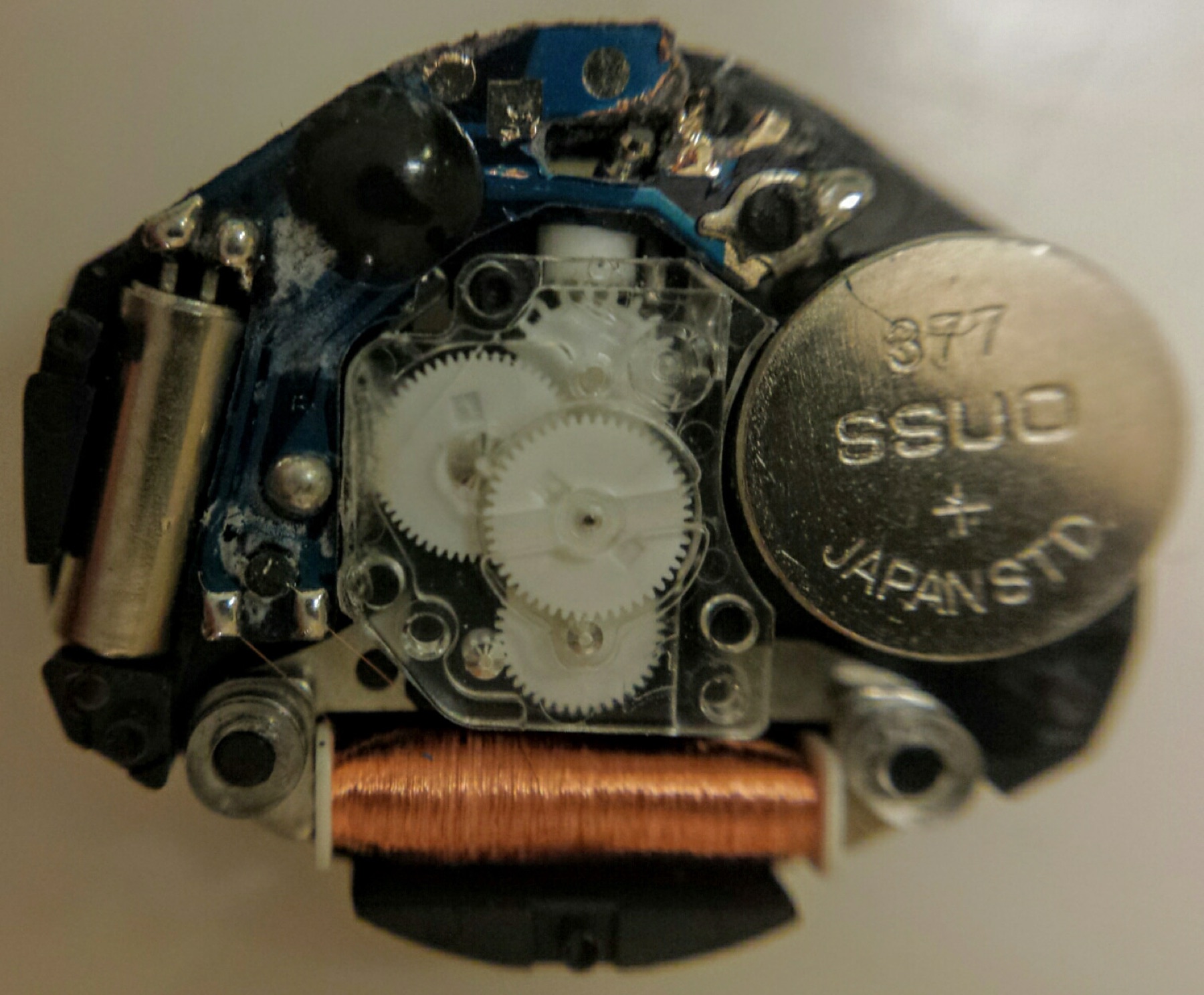 Open quartz watch movement showing its battery, coil, electronic components and gear train
