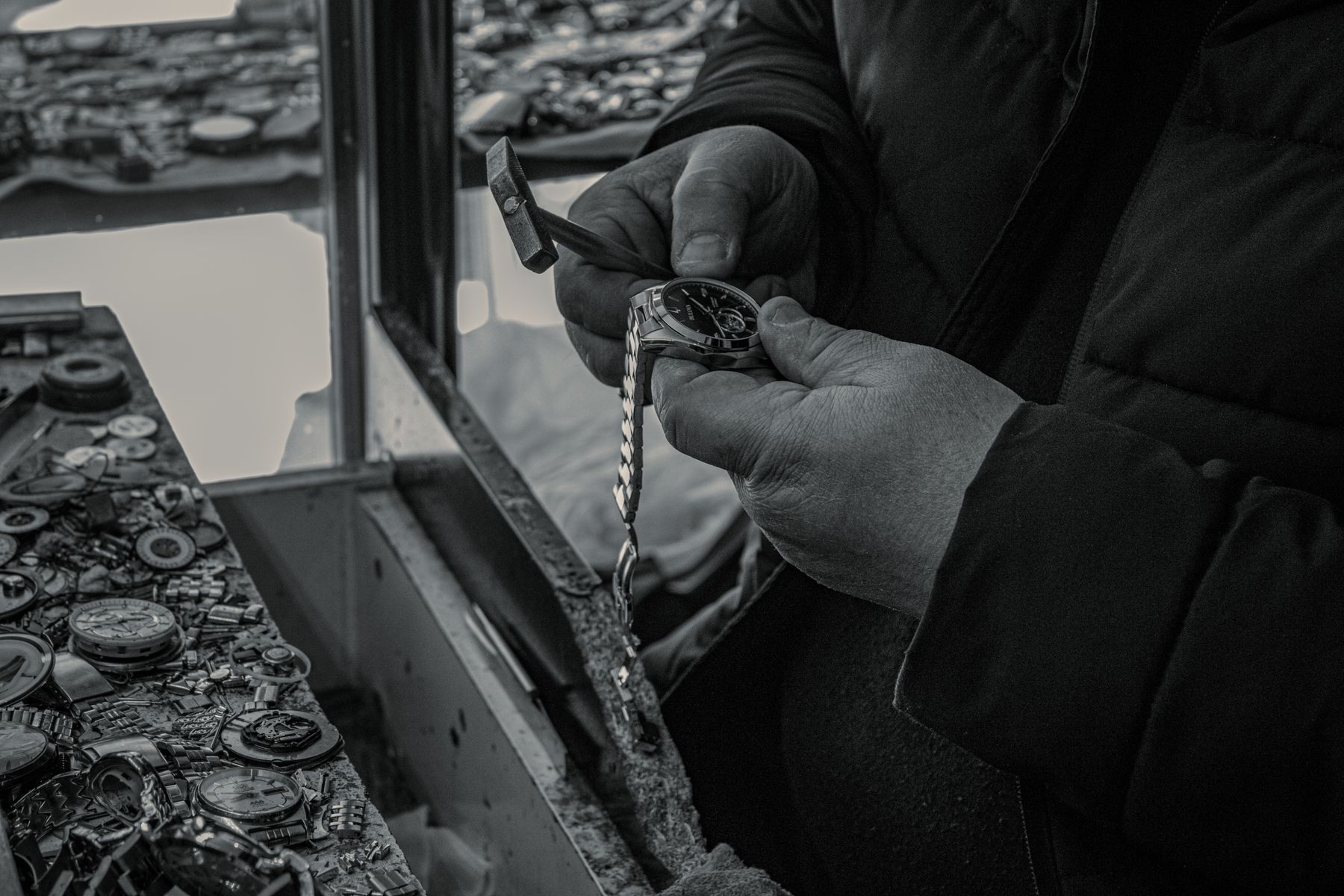 Watchmaker holding a wristwatch at a workbench surrounded by watch parts